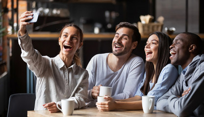 Cheerful diverse millennial friends taking selfie on smartphone in cafe