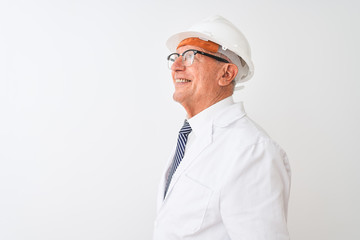 Senior grey-haired engineer man wearing coat and helmet over isolated white background looking to side, relax profile pose with natural face with confident smile.