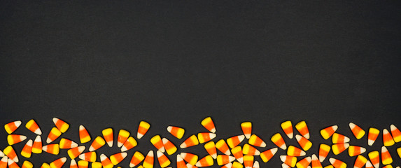 Halloween candy corn bottom border banner. Top view on a black background with copy space.