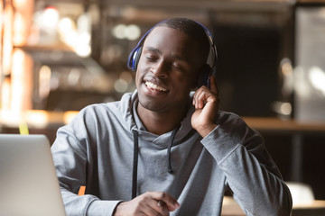 Relaxed young black man wear wireless headphones enjoy good music
