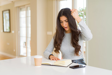 Young woman reading a book and drinking a coffe annoyed and frustrated shouting with anger, crazy...