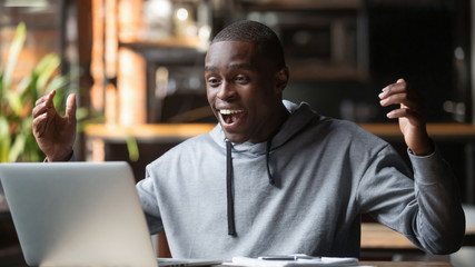 Overjoyed african man read great news online look at laptop