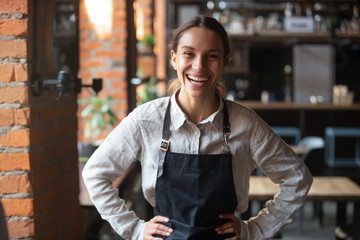 Cheerful young waitress wearing apron laughing looking at camera - obrazy, fototapety, plakaty
