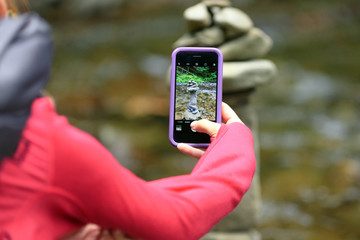 Girl taking photos of the stones in the mountains using the phone. Close-up shot of the hand holding the phone with the stones behind.