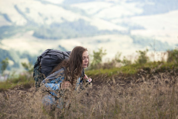 Girl hiker with a backpack climbing up a mountain