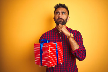 Arab indian hispanic man holding birthday gift standing over isolated yellow background serious...