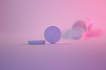 White round tablet near lies.One pill stands on the rib next to it. In the background, pills are spilled out of a jar.  The concept of treatment, medications, disease