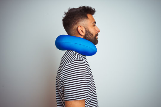 Young indian tourist man on travel wearing neckpillow over isolated white background looking to side, relax profile pose with natural face with confident smile.