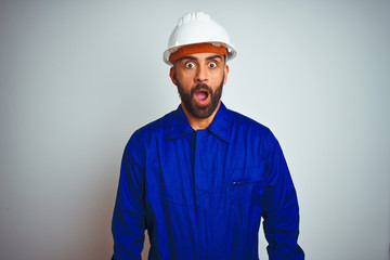 Handsome indian worker man wearing uniform and helmet over isolated white background afraid and shocked with surprise expression, fear and excited face.