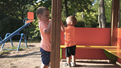 Fototapeta premium Two little boys playing on the playground with swing on the background