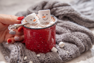 Red mug with hot chocolate with melted marshmallow snowman in a woman hands