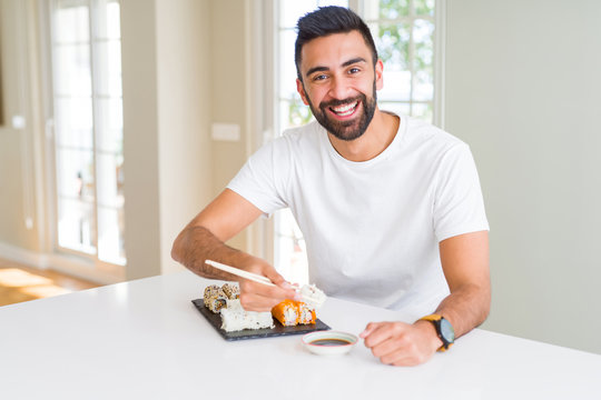 Handsome man smiling happy enjoying eating fresh colorful asian sushi using chopsticks