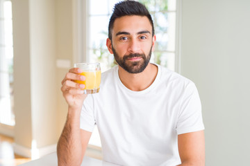 Handsome hispanic man drinking healthy orange juice with a confident expression on smart face thinking serious
