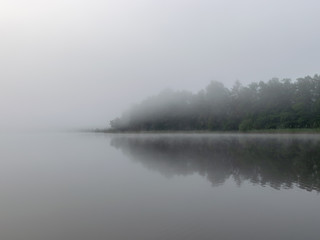 blurred lake in the background and tree silhouettes, thick mist on the lake, Lielezers lake in Augstroze, Latvia