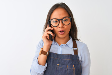 Chinese woman wearing glasses apron talking on smartphone over isolated white background scared in shock with a surprise face, afraid and excited with fear expression