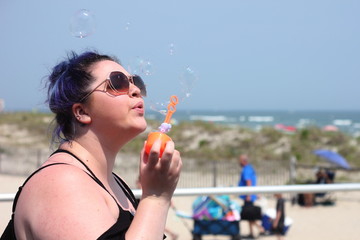 Side view of young woman blowing bubbles by the beach