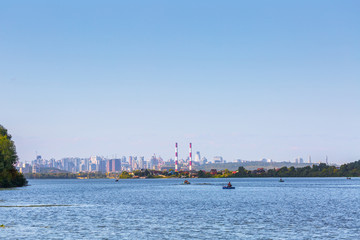 Summer sunny hot evening. Modern residential areas southern suburbs and midtown on hills in Kyiv on the right bank of the Dnipro River. Fishermen on boats on foreground. Kyiv. Ukraine. Aug. 28, 2019