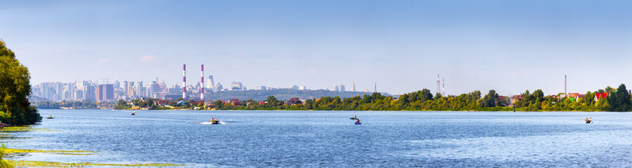 Fototapeta na wymiar Summer sunny hot evening. Modern residential areas southern suburbs and midtown on hills in Kyiv on the right bank of the Dnipro River. Fishermen on boats on foreground. Kyiv. Ukraine. Aug. 28, 2019