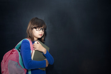 Back to school concept. Happy schoolgirl with backpack and books at the black chalkboard in classroom