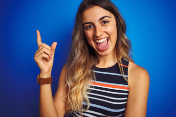 Young beautiful woman wearing stripes t-shirt over blue isolated background very happy pointing with hand and finger to the side