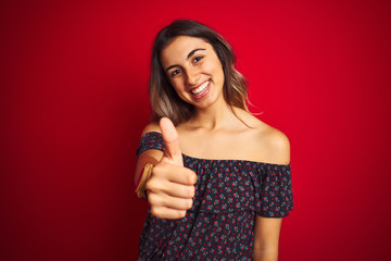 Young beautiful woman wearing a floral t-shirt over red isolated background doing happy thumbs up gesture with hand. Approving expression looking at the camera with showing success.