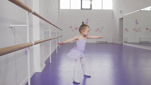 Cute little ballerina whirling in dance at ballet school. Adorable little girl learning dancing at ballet class. Ballerina girl in violet leotard and skirt whirls. Childhood, activities concept
