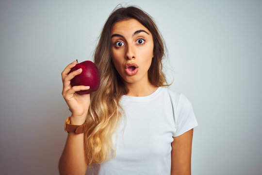 Young beautiful woman eating red apple over grey isolated background scared in shock with a surprise face, afraid and excited with fear expression