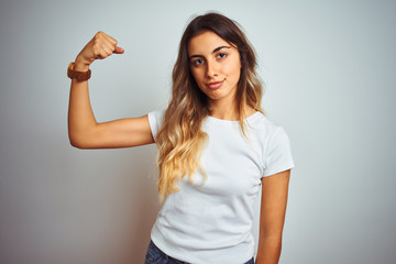 Young beautiful woman wearing casual white t-shirt over isolated background Strong person showing arm muscle, confident and proud of power