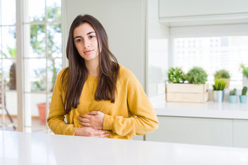 Beautiful young woman wearing yellow sweater with hand on stomach because nausea, painful disease...