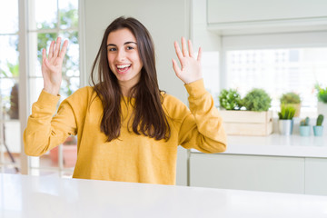 Beautiful young woman wearing yellow sweater showing and pointing up with fingers number nine while smiling confident and happy.