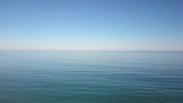 Aerial view of drone flight above calm and tranquil turquoise ocean water, with blue sky and horizon as background.