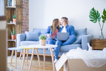 Young couple relaxing sitting on the sofa using the computer laptop around cardboard boxes, very happy moving to a new house