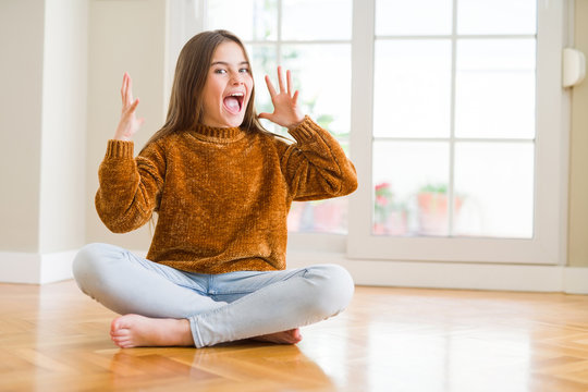 Beautiful young girl kid sitting on the floor at home celebrating crazy and amazed for success with arms raised and open eyes screaming excited. Winner concept