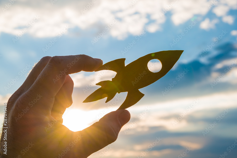 Wall mural Rocket in hand on a background of the sky of the sun at sunset. On your marks. Concept business idea, success, take-off, promotion.