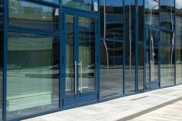 Diagonal view of modern building wall with bif glass window and door with blue frame. Street reflection.