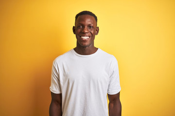 Young african american man wearing white t-shirt standing over isolated yellow background with a happy and cool smile on face. Lucky person.