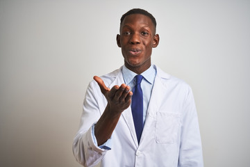 Young african american doctor man wearing coat standing over isolated white background looking at the camera blowing a kiss with hand on air being lovely and sexy. Love expression.