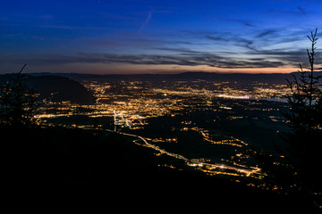 Evening top view of city lights, French Annemasse, Swiss Geneva,lake Geneva and picturesque sky with dark clouds after sunset,photo with long exposure.Department of Haute-Savoie in France.