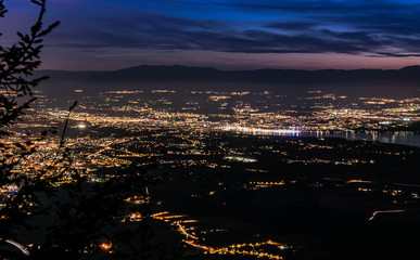 Fototapeta na wymiar Evening top view of city lights, French Annemasse, Swiss Geneva,lake Geneva and picturesque sky with dark clouds after sunset,photo with long exposure.Department of Haute-Savoie in France.