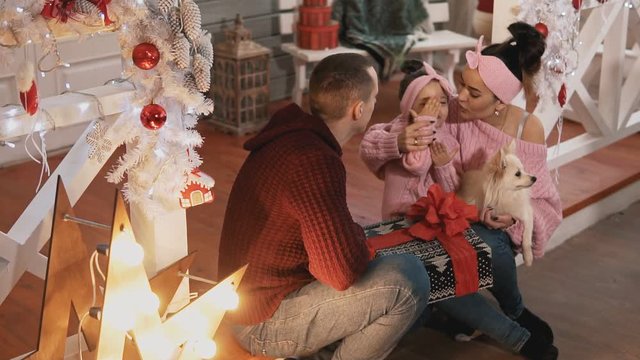 Young family in pullovers hugging in Christmas day. Smiling family with little daughter and dog having fun together. Happy family concept. Medium shot