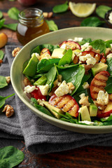 Summer Peach Salad with spinach, avocado, walnuts and feta cheese in rustic bowl. healthy food.