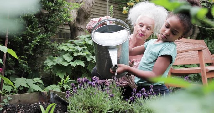 Grandmother helping grandchild water the garden