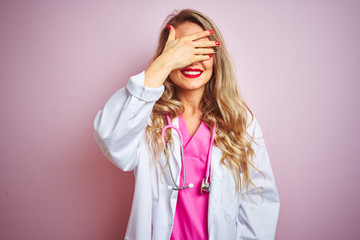 Young beautiful doctor woman using stethoscope over pink isolated background smiling and laughing with hand on face covering eyes for surprise. Blind concept.