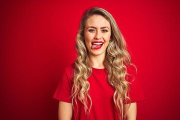 Young beautiful woman wearing basic t-shirt standing over red isolated background sticking tongue out happy with funny expression. Emotion concept.