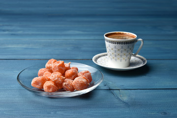 Morning black coffee in a cup and dried kumquats in powdered sugar on a blue background