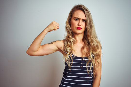 Young beautiful woman wearing stripes t-shirt standing over white isolated background Strong person showing arm muscle, confident and proud of power
