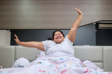 Happy fat woman stretching hands after wake up
