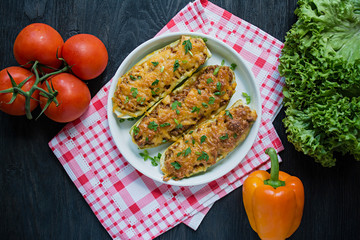 Stuffed zucchini with minced meat and grated cheese in a glass baking sheet. Dark wooden background.