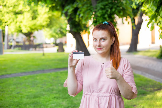 Young Caucasian Woman Stay In Park And Show White Credit Card With Black Magnet Line. Shopping And Retail Concept. Plastic Bank-card Design Mock Up