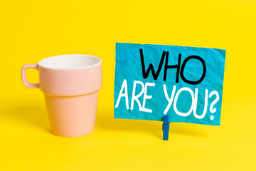 Handwriting text Who Are You Question. Conceptual photo asking about someone identity or demonstratingal information Cup empty paper blue clothespin rectangle shaped reminder yellow office